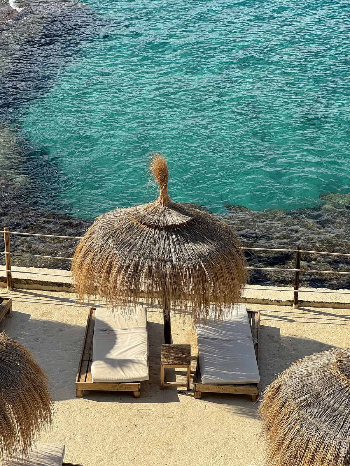 An image of a thatched umbrella and subbed set against bright blue water at Gran Folies