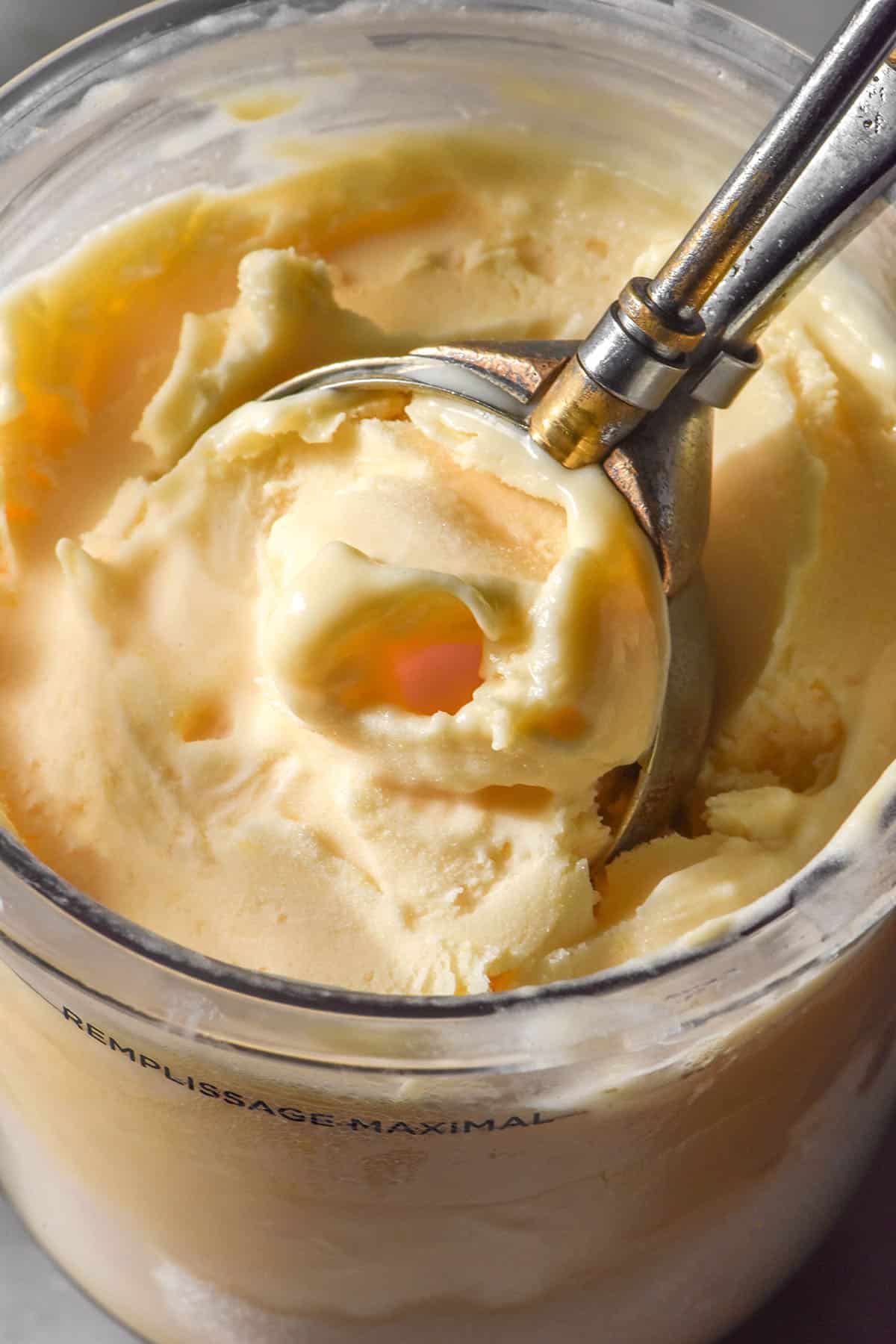 A close up macro image of a scoop of ice cream being taken from a tub of Ninja Creami lemon curd ice cream