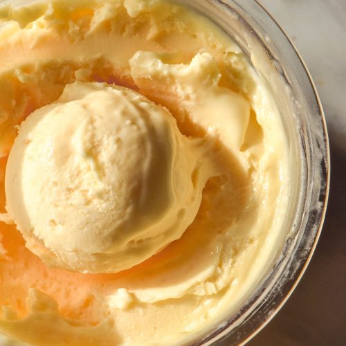 An aerial macro image of a tub of Ninja Creami lemon curd ice cream on a white marble table