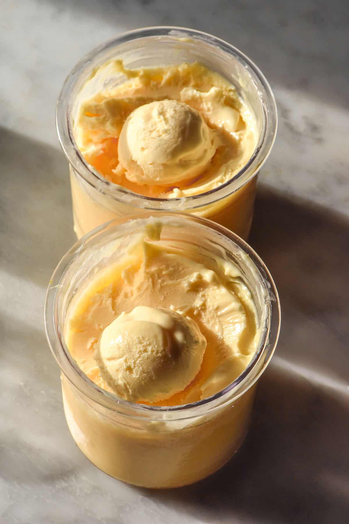 A side on image of two tubs of Ninja Creami lemon curd ice cream on a white marble table