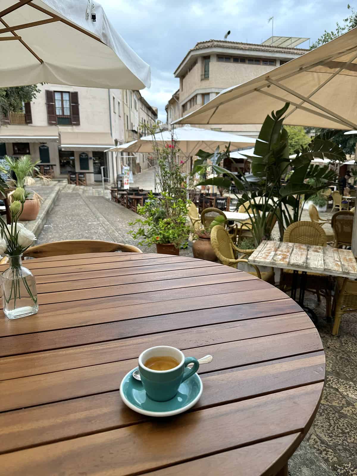 A view of the square as seen from Bo's Pollenca. An espresso on a table sits in the foreground while other restaurants fill the square 