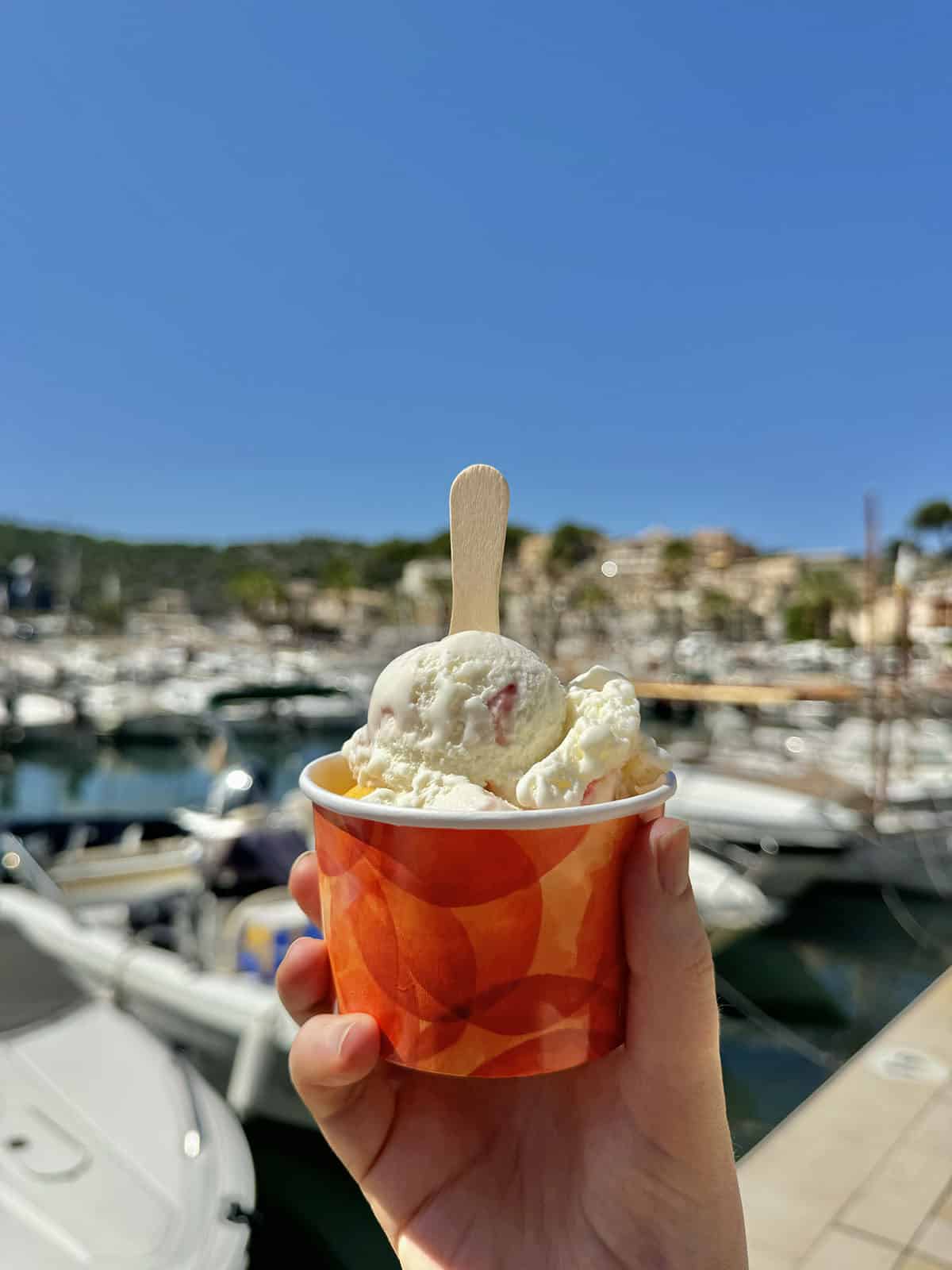 An image of an ice cream held up against the port filled with boats at Port De Soller