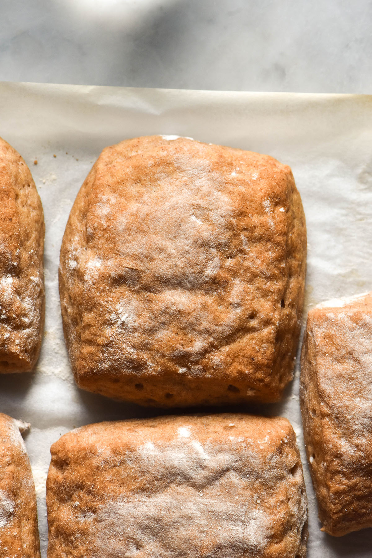 A close up aerial image of gluten free ciabatta rolls on a sheet of baking paper atop a white marble table