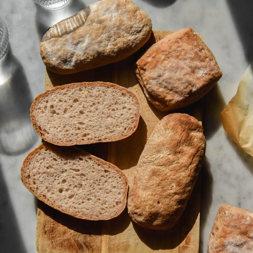 An aerial image of gluten free ciabatta in various sizes casually arranged on a sunlit white marble table