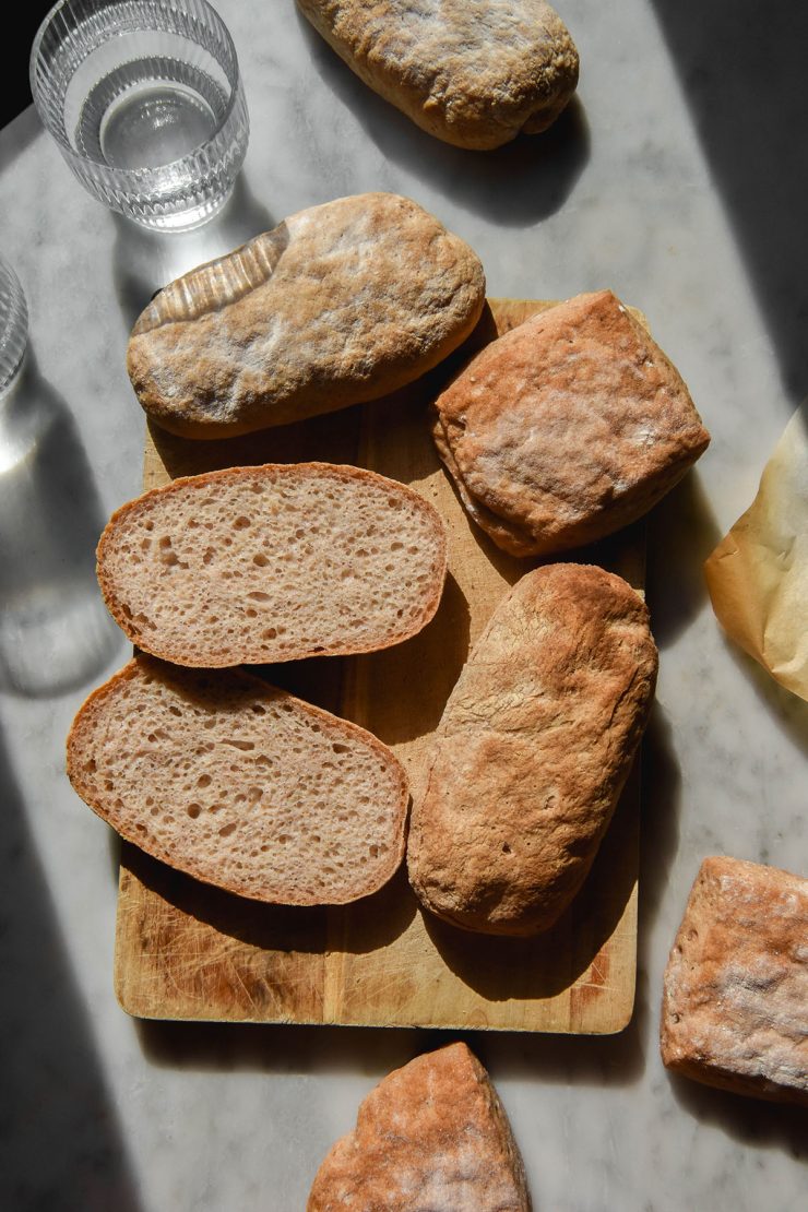 An aerial image of gluten free ciabatta in various sizes casually arranged on a sunlit white marble table