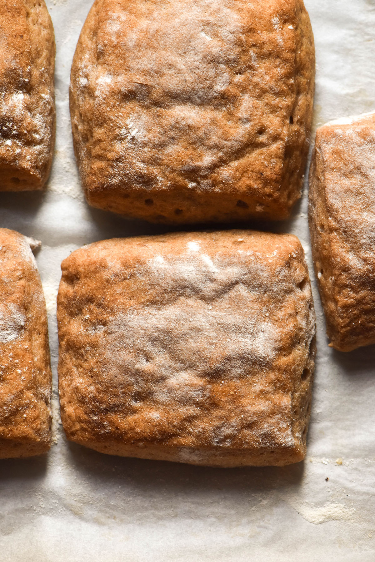 A brightly lit aerial image of gluten free ciabatta rolls on a sheet of baking paper