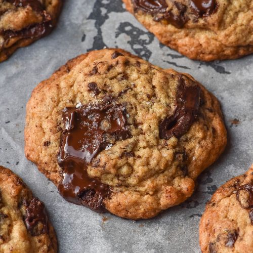 A side on image of gluten free banana cookies with molten chocolate chunks on a lined baking tray