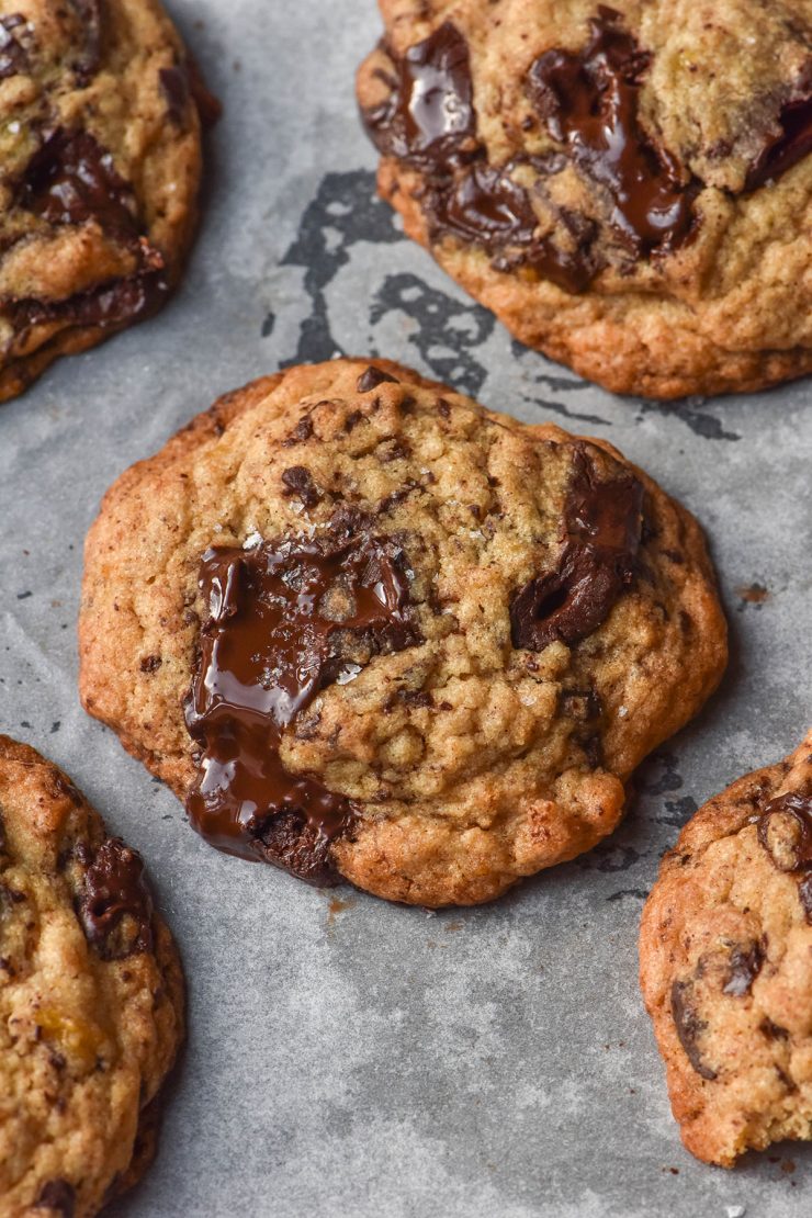 A side on image of gluten free banana cookies with molten chocolate chunks on a lined baking tray