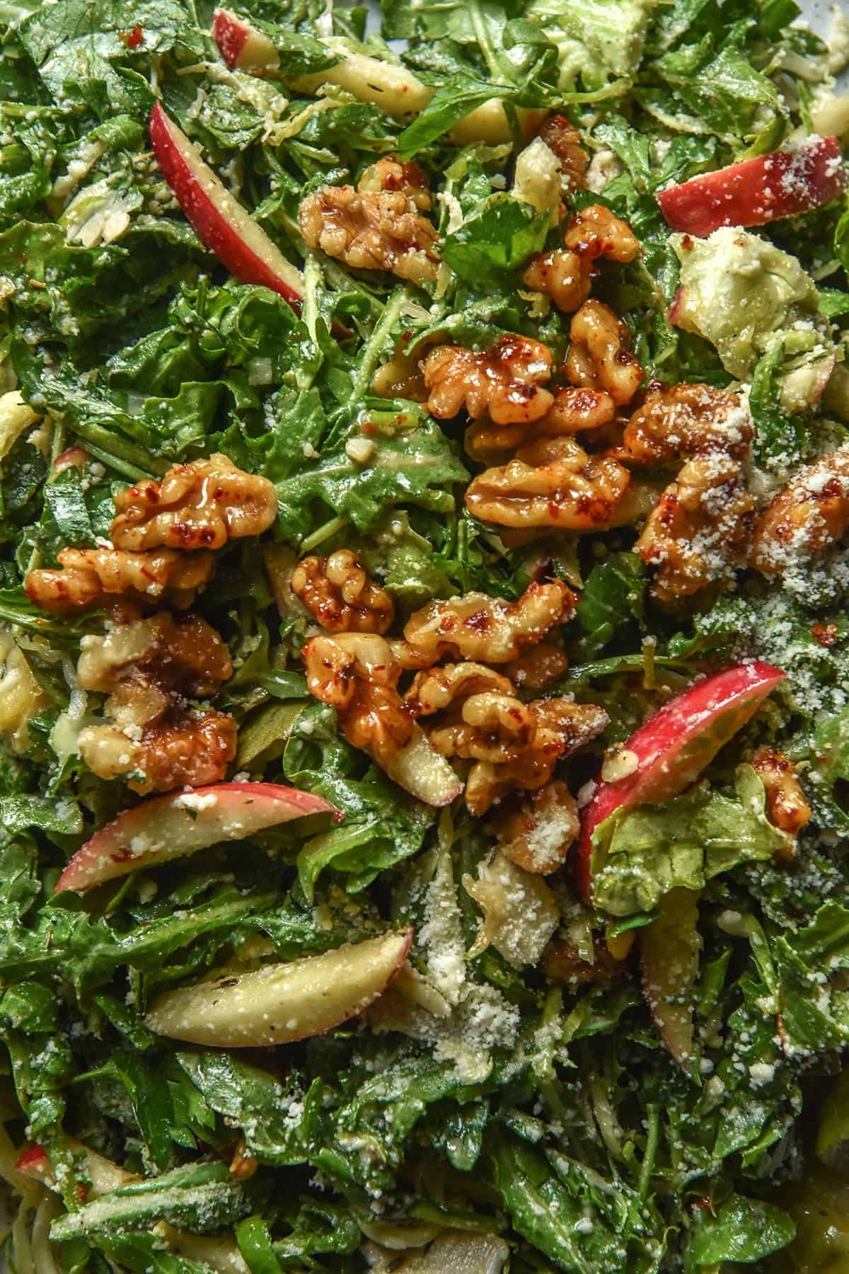 An aerial macro close up image of a lower FODMAP shaved Brussels sprout salad with rocket, red apple, maple chilli walnuts and a sprinkling of parmesan