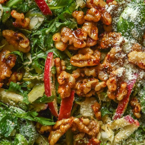 A macro aerial close up image of a lower FODMAP shaved Brussels sprout salad with rocket, red apple, maple chilli walnuts and a sprinkling of parmesan