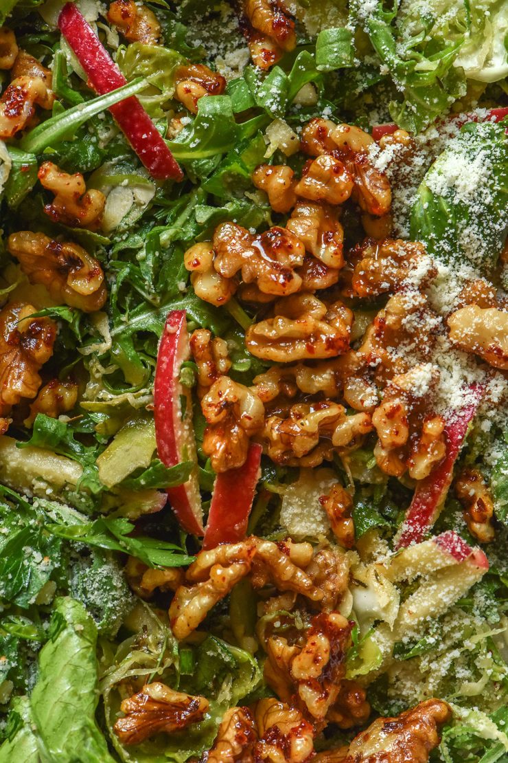 A macro aerial close up image of a lower FODMAP shaved Brussels sprout salad with rocket, red apple, maple chilli walnuts and a sprinkling of parmesan