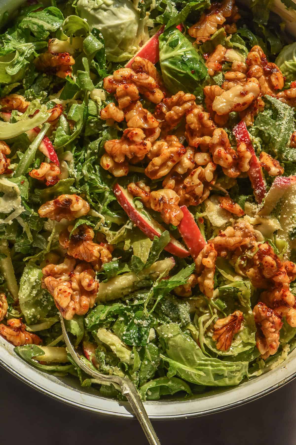 A brightly lit aerial image of a lower FODMAP shaved Brussels sprout salad with rocket, red apple, maple chilli walnuts and a sprinkling of parmesan