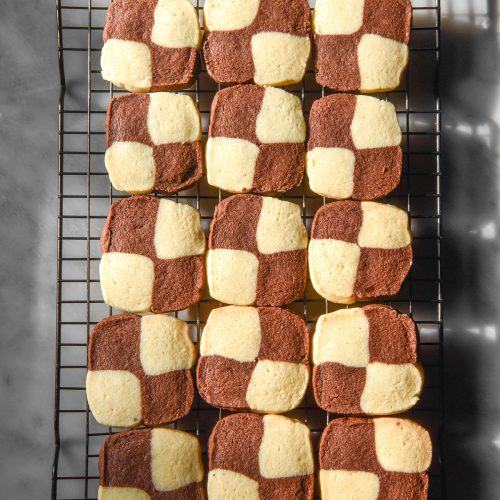 An aerial sunlit image of gluten free chocolate and vanilla checkerboard cookies on a cooling rack atop a white marble table