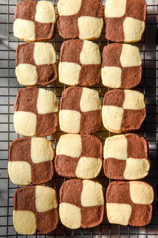 An aerial sunlit image of gluten free chocolate and vanilla checkerboard cookies on a cooling rack atop a white marble table