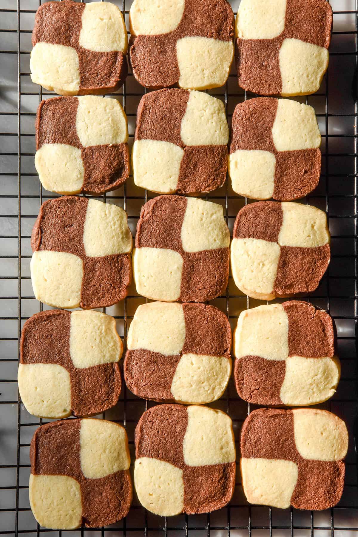 An aerial sunlit image of gluten free chocolate and vanilla checkerboard cookies on a cooling rack atop a white marble table