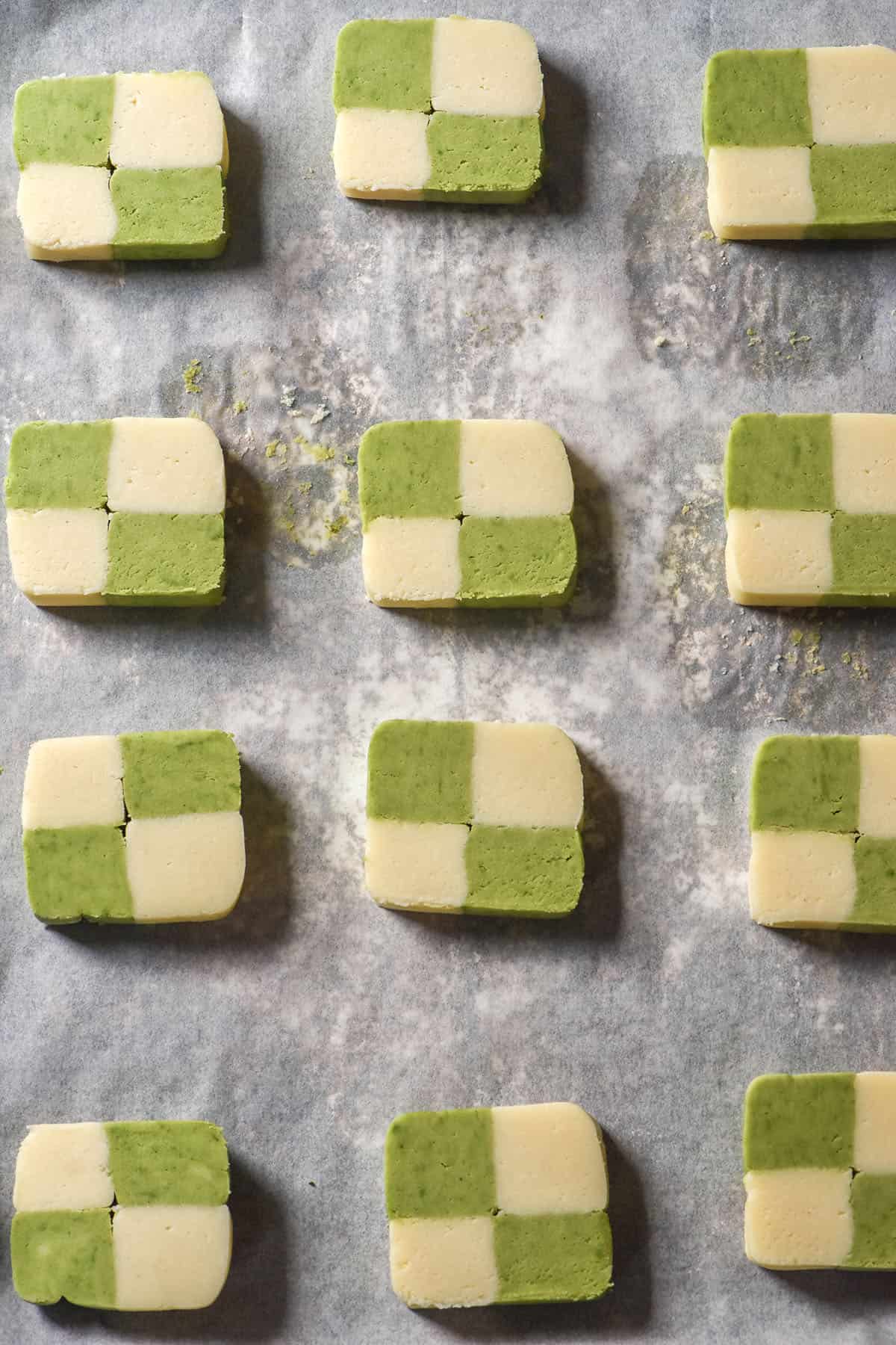 An aerial image of unbaked gluten free vanilla and matcha checkerboard cookies on a lined baking tray