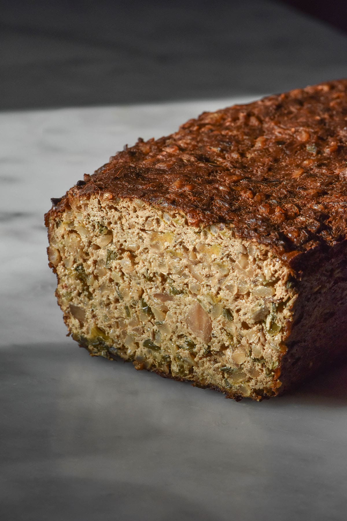 A side on image of a gluten free vegan meatloaf on a white marble table. The meat loaf has been sliced to reveal the inner texture of the loaf