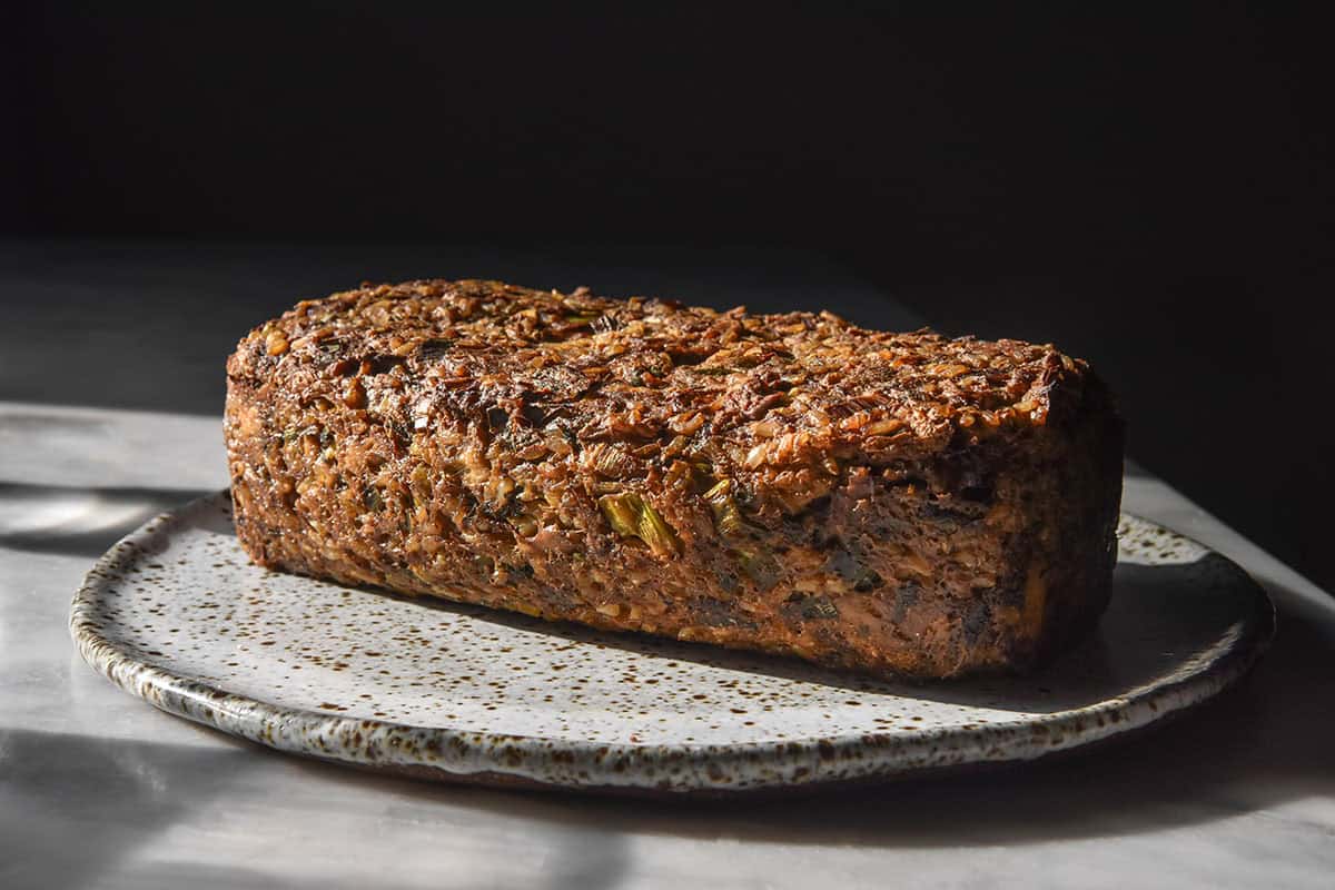 A side on image of a gluten free low FODMAP vegan meatloaf on a white speckled ceramic plate against a dark backdrop