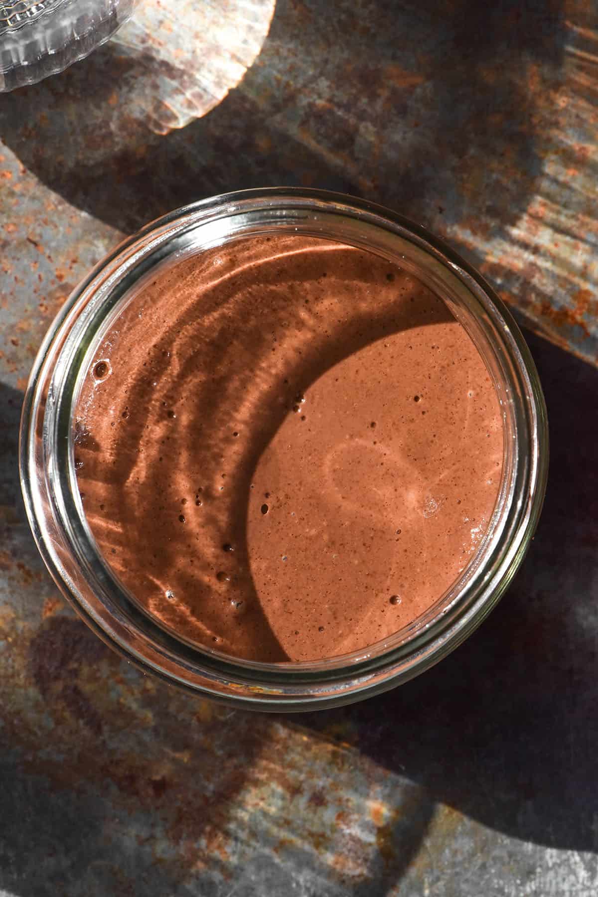 An aerial image of a blended chocolate chia pudding on a steel backdrop surrounded by sunlit water glasses