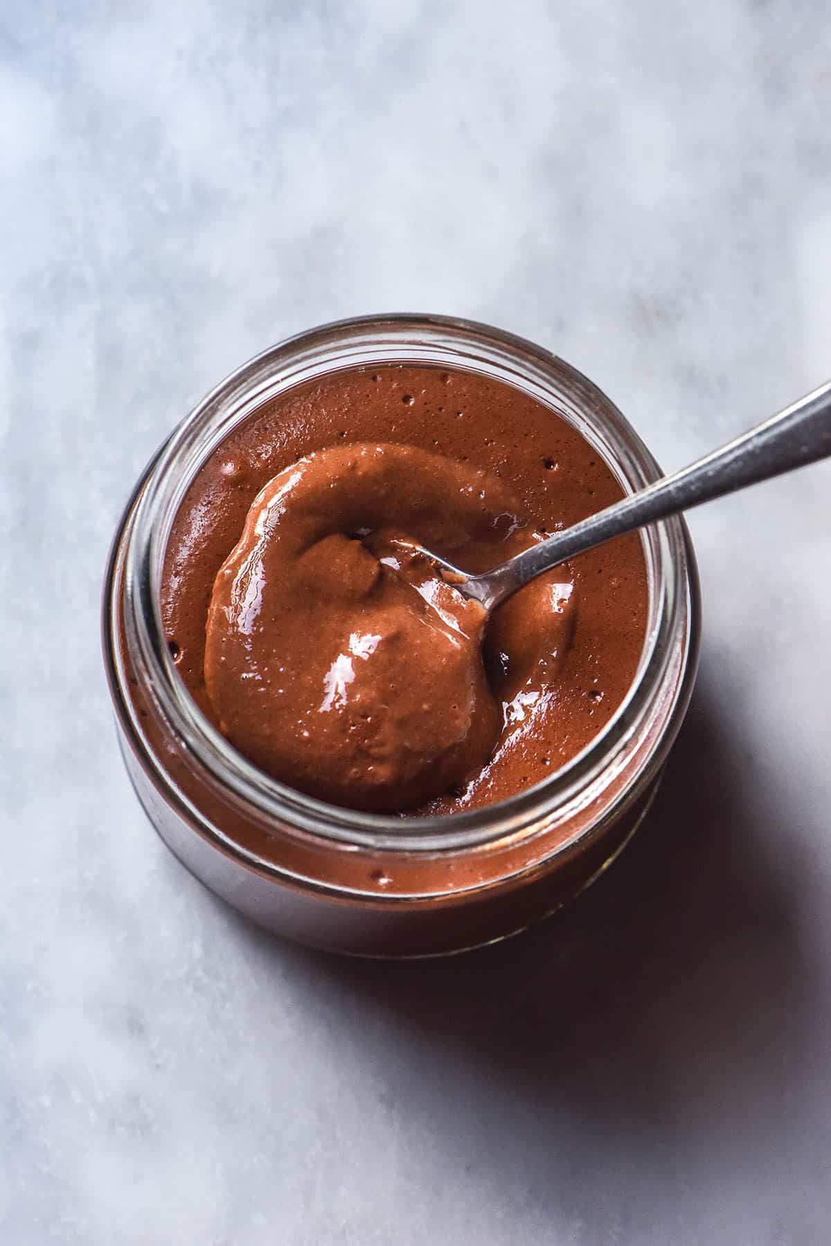 An aerial image of a glass jar filled with blended chocolate chia pudding atop a white marble table