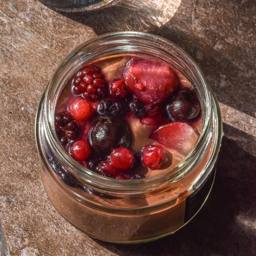 A brightly lit image of a blended chocolate chia pudding on a dark brown backdrop surrounded by sunlit water glasses