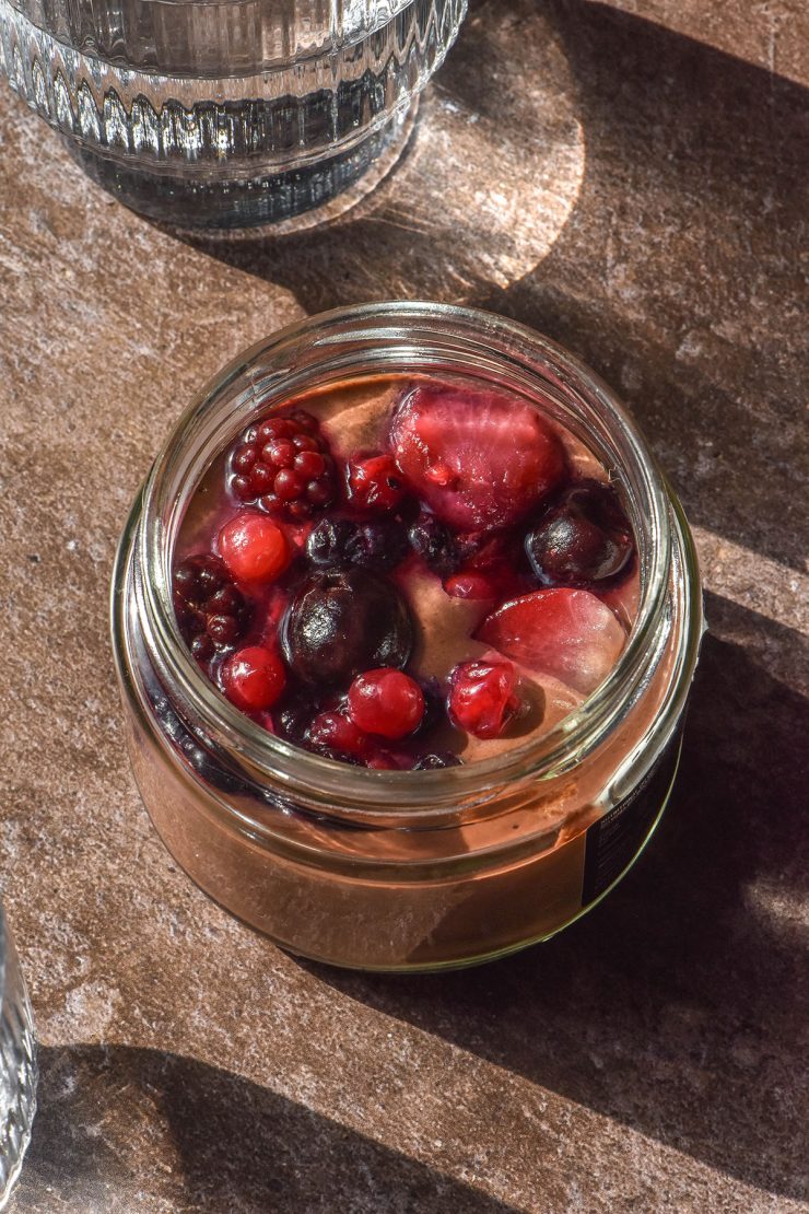 A brightly lit image of a blended chocolate chia pudding on a dark brown backdrop surrounded by sunlit water glasses