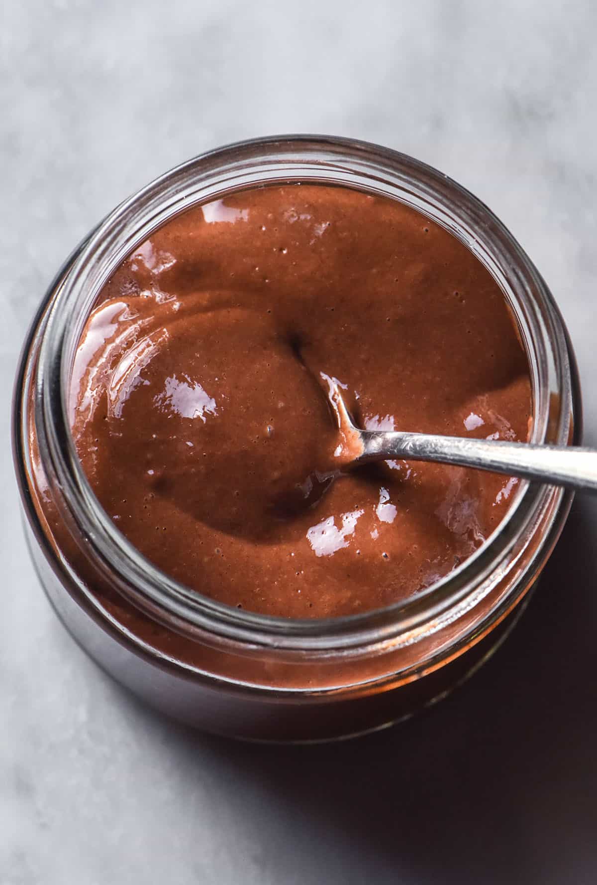 A close up aerial image of a blended chocolate chia pudding in a glass jar atop a white marble table.