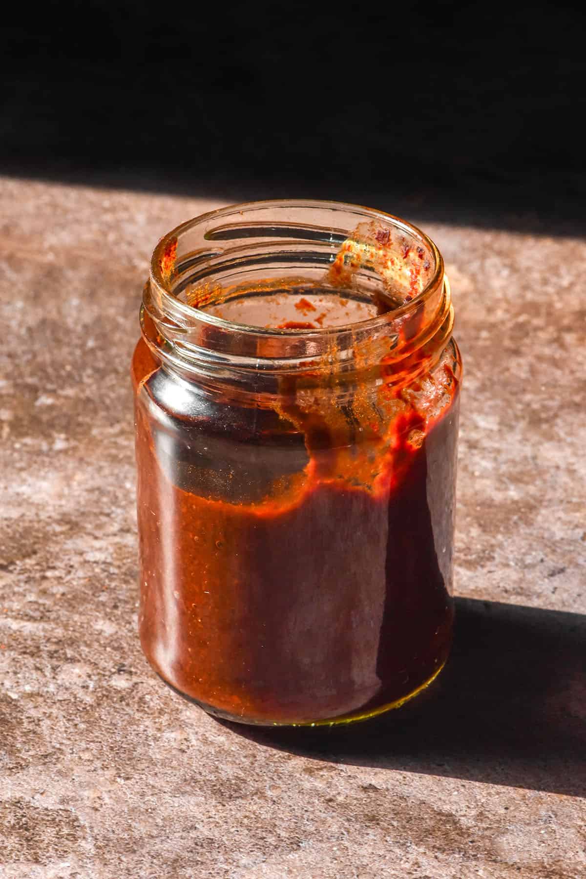 A sunlit glass jar filled with gluten free gochujang against a brown backdrop