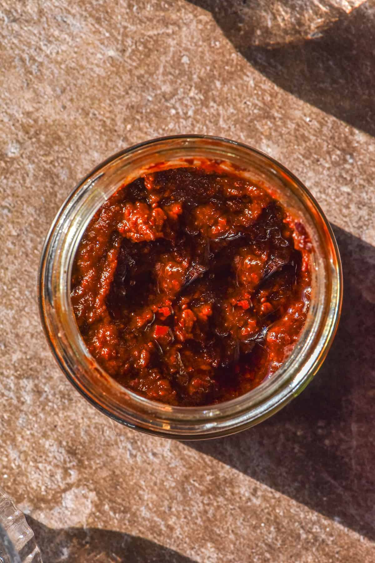 An aerial image of a glass jar filled with gluten free gochujang atop a dark brown backdrop