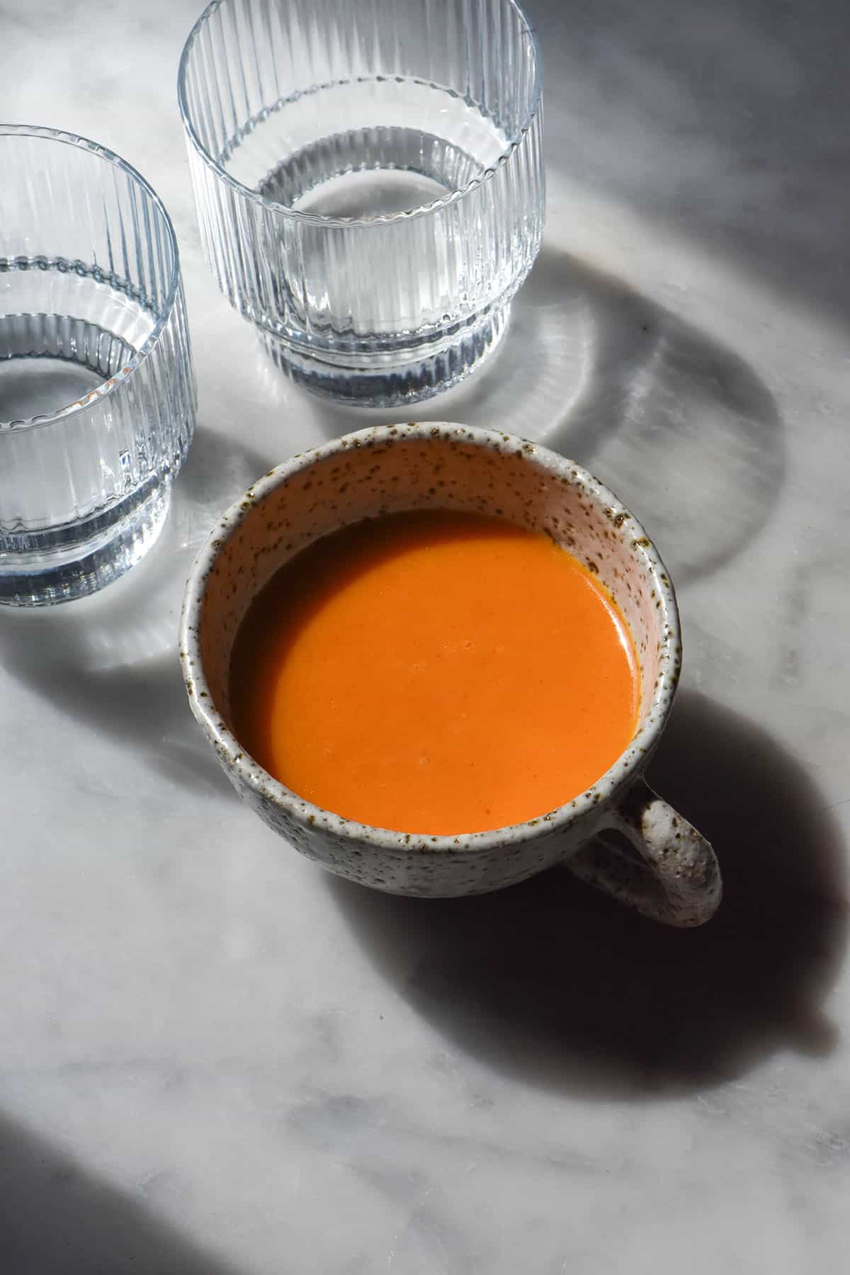 An aerial sunlit image of white ceramic mug filled with low FODMAP Buffalo sauce on a white marble table. 