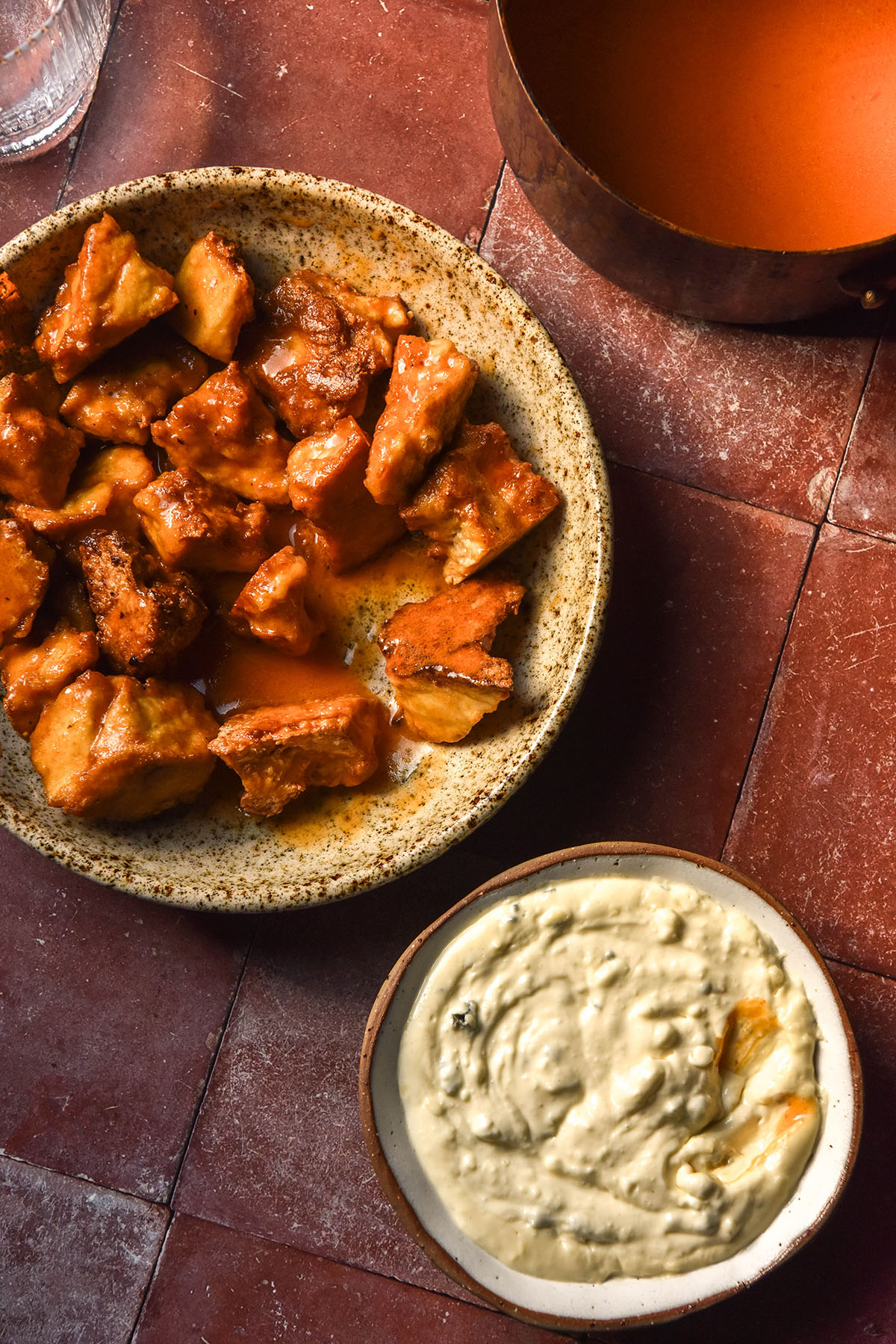 An aerial image of Buffalo Tofu, low FODMAP Buffalo sauce and low FODMAP blue cheese dip casually arranged on a terracotta tile backdrop