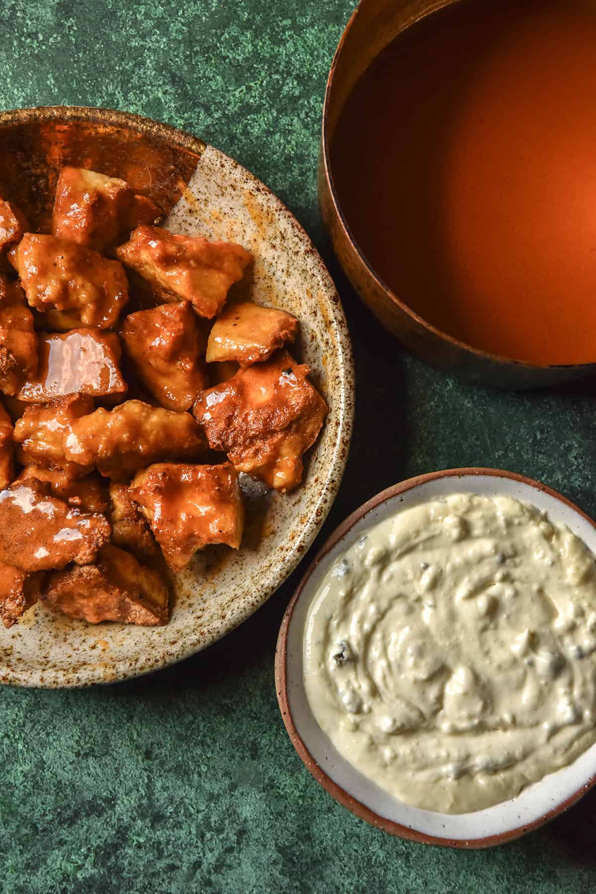 An aerial image of low FODMAP blue cheese dip, Buffalo tofu and low FODMAP Buffalo sauce atop an olive green backdrop