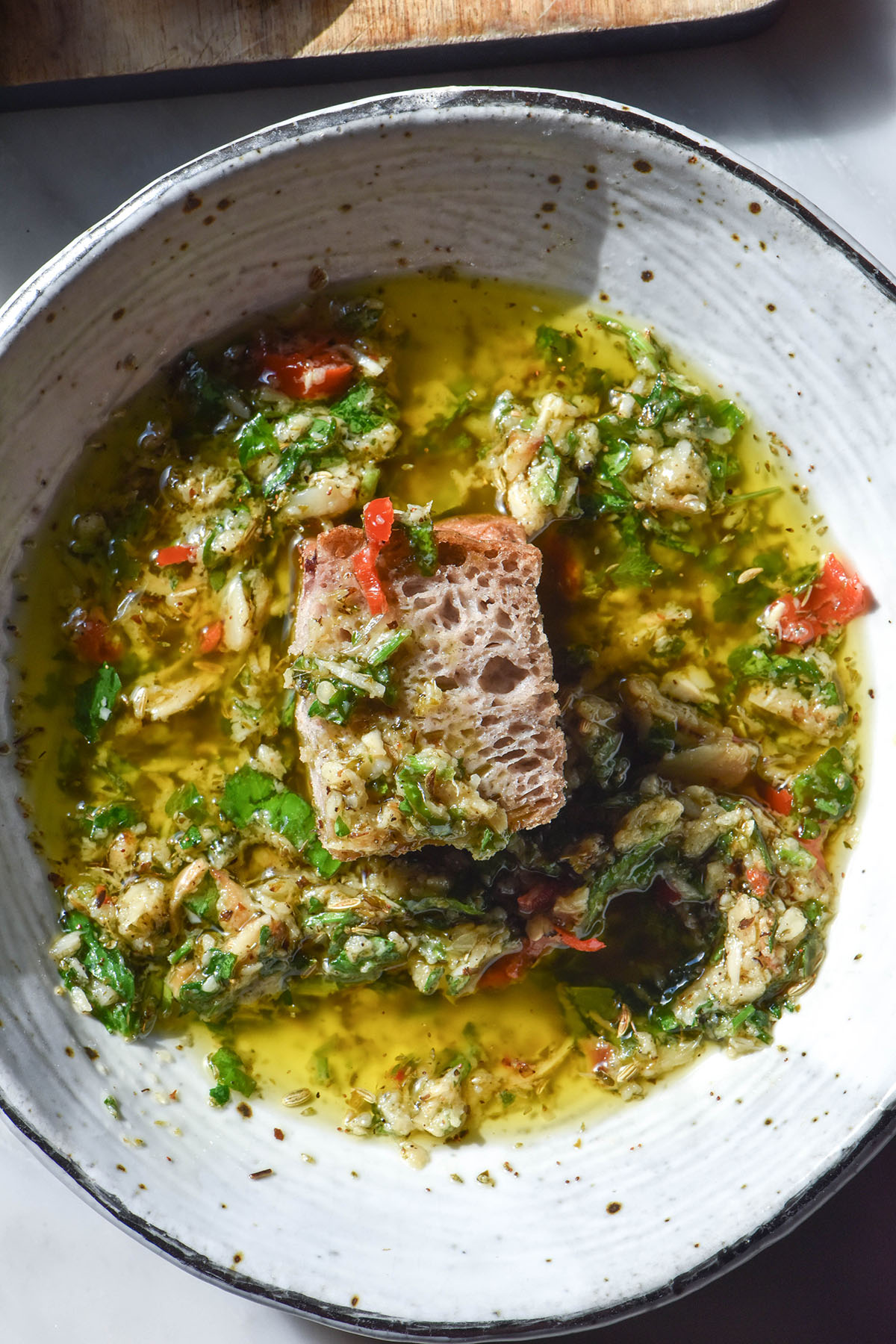 An aerial image of a white ceramic bowl filled with low FODMAP bread dipping oil. In the centre of the bowl is a piece of gluten free buckwheat focaccia