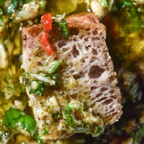 An aerial macro image of a piece of gluten free buckwheat focaccia submerged in a bowl of low FODMAP bread dipping oil