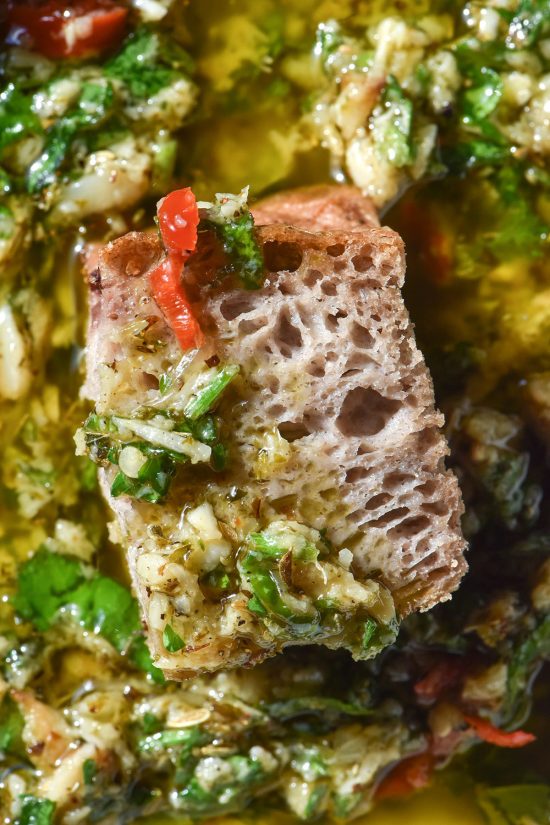 An aerial macro image of a piece of gluten free buckwheat focaccia submerged in a bowl of low FODMAP bread dipping oil