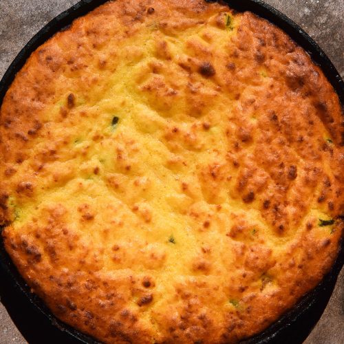 A sunlit aerial image of a low FODMAP cornbread chilli in a black skillet atop a speckled brown backdrop