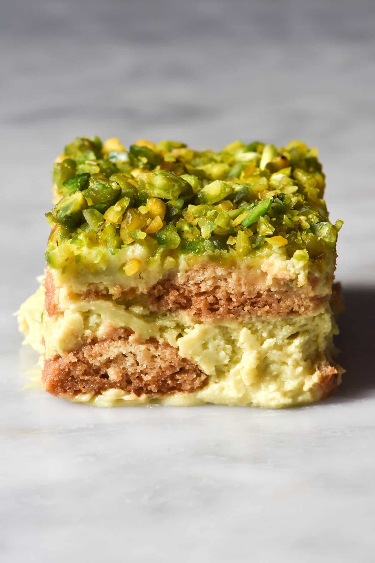 A close up of a slice of gluten free Pistachio Tiramisu on a white marble table