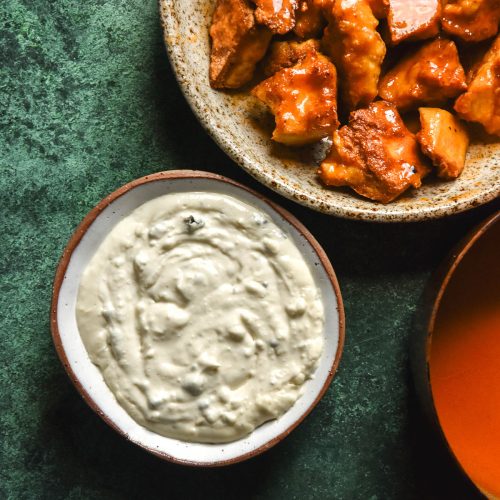 An aerial image of low FODMAP blue cheese dip and tofu buffalo nuggets on an olive green backdrop