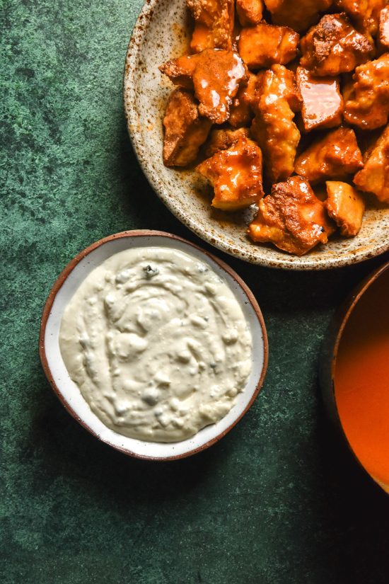 An aerial image of low FODMAP blue cheese dip and tofu buffalo nuggets on an olive green backdrop