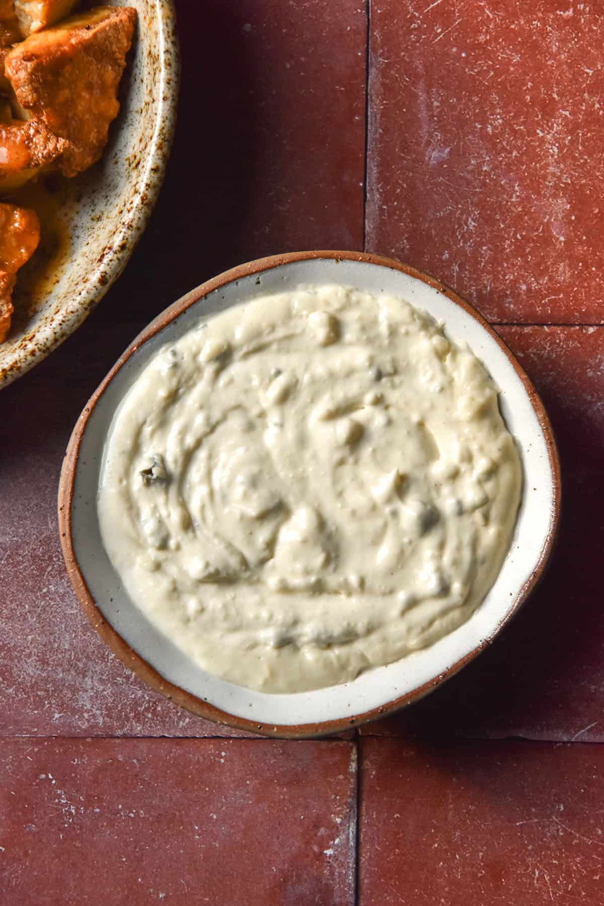 An aerial image of a white ceramic dish filled with low FODMAP blue cheese dip on a terracotta tile backdrop