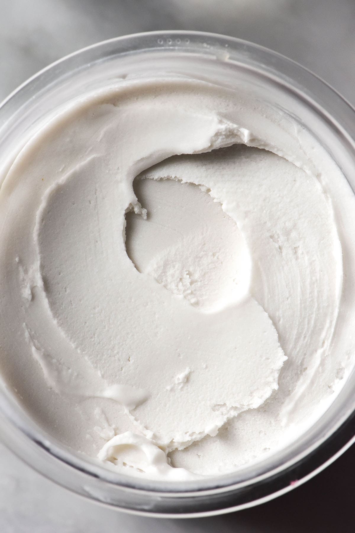 An aerial close up image of a tub of Ninja Creami coconut ice cream on a white marble table. 