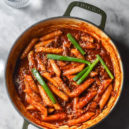 An aerial image of a skillet filled with vegan gluten free tteokbokki on a white marble table.