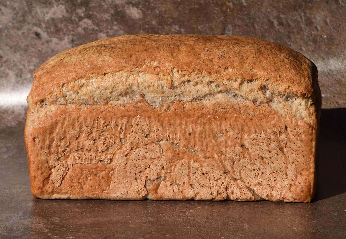 A side on shot of a loaf of gluten free yeast free bread on a light brown backdrop