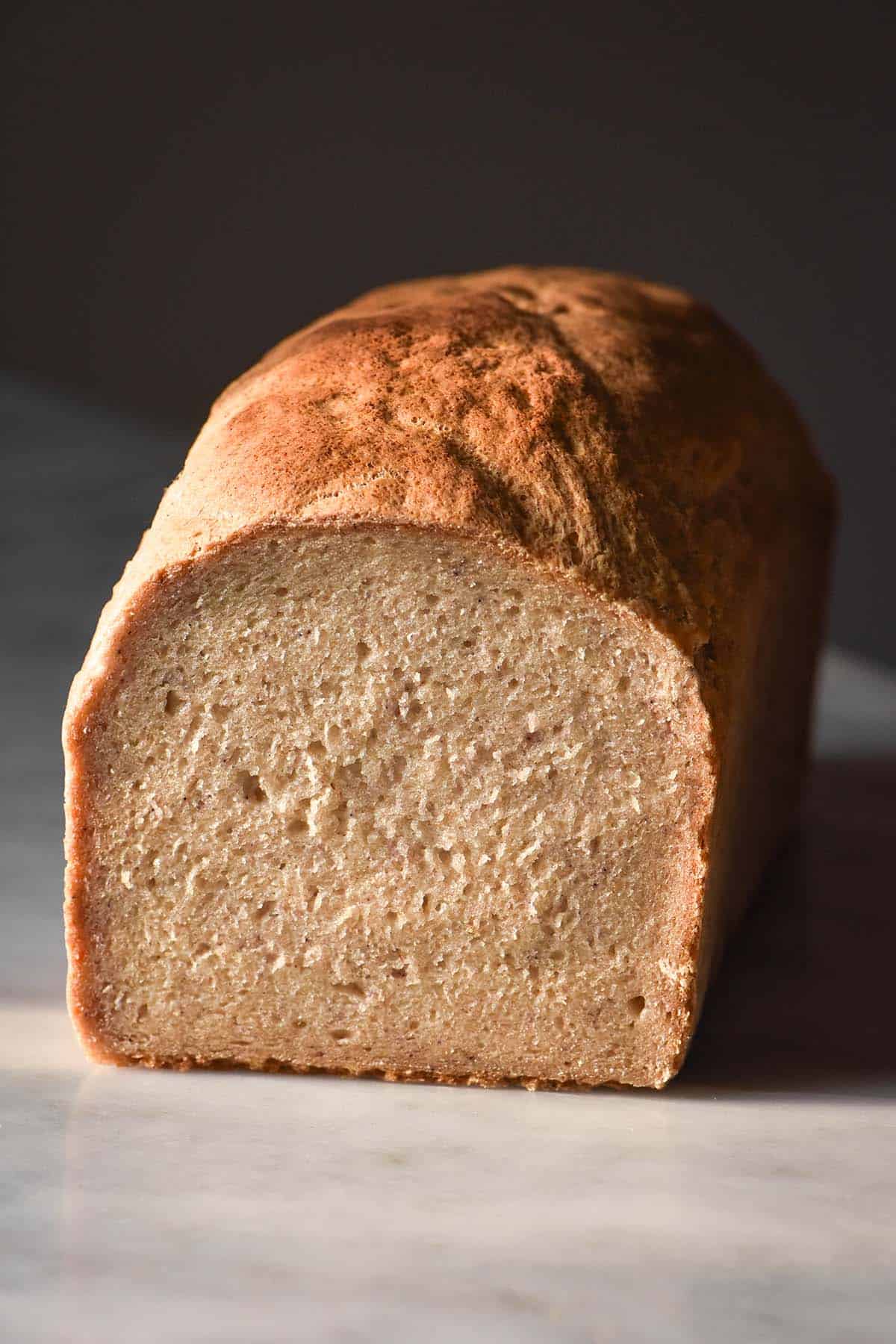 An image of a loaf of gluten free vegan yeast free bread on a white marble table against a dark backdrop. The loaf has been sliced to reveal the crumb inside. 