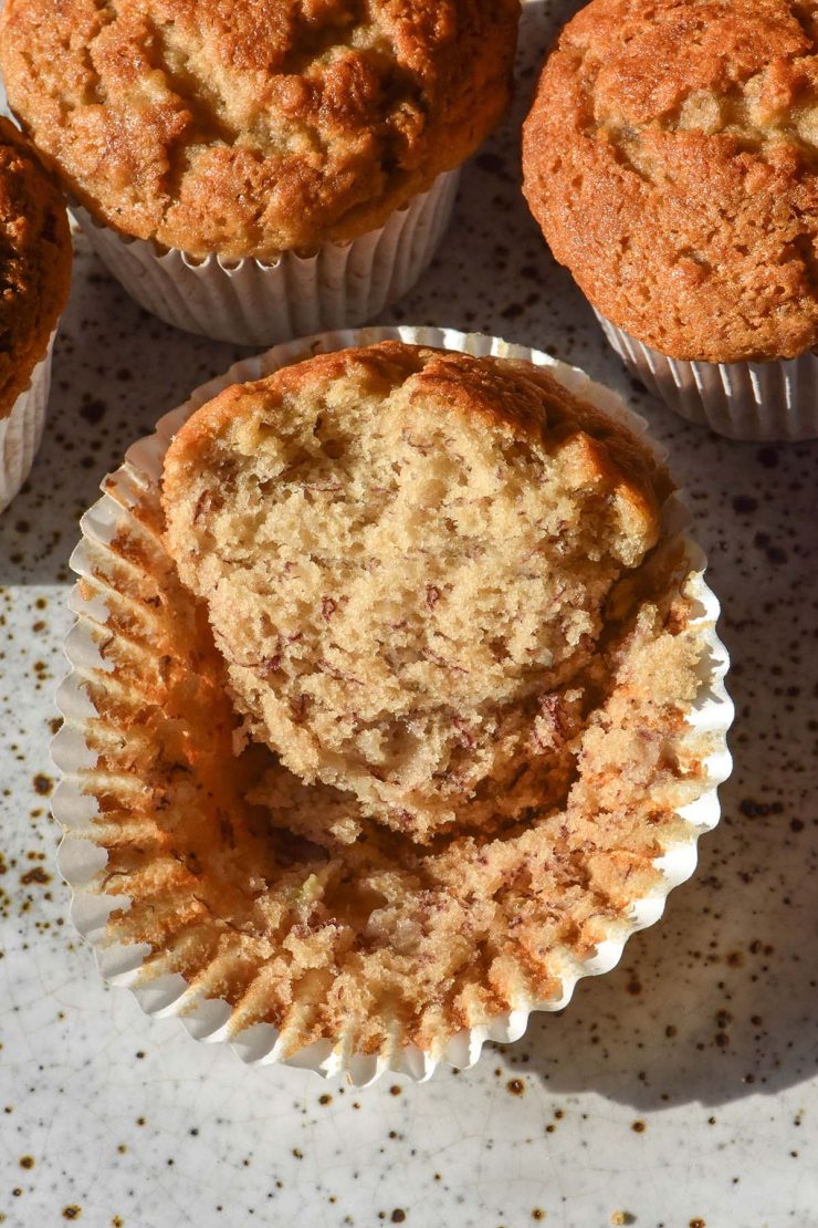 An aerial image of a fluffy gluten free vegan muffin on a white speckled ceramic plate