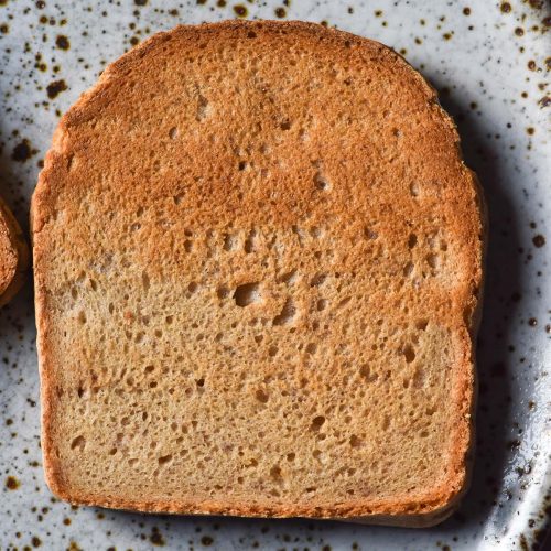 An aerial image of a slice of gluten free yeast free toast atop a white speckled ceramic plate