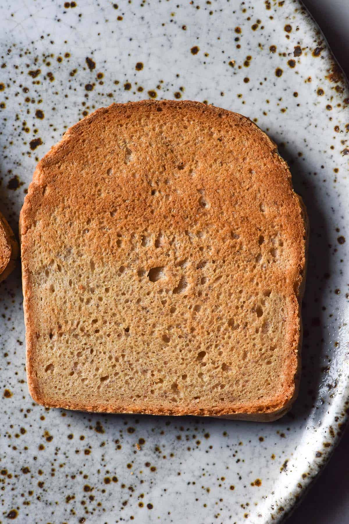 An aerial image of a slice of gluten free yeast free toast atop a white speckled ceramic plate