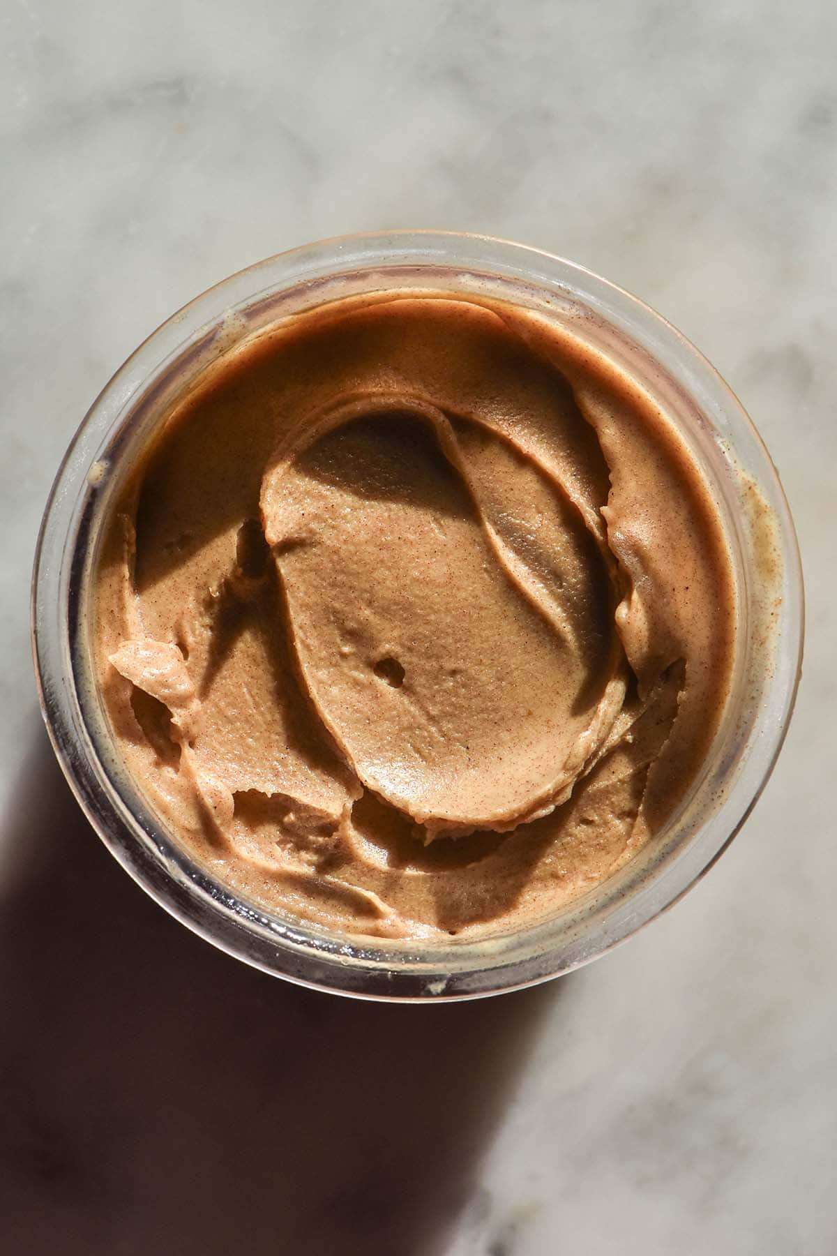 An aerial sunlit image of a tub of high protein sticky date Ninja Creami ice cream atop a white marble table