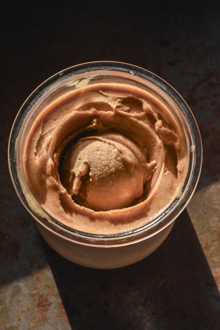 A dark and moody aerial image of a tub of Ninja Creami sticky date pudding atop a dark backdrop