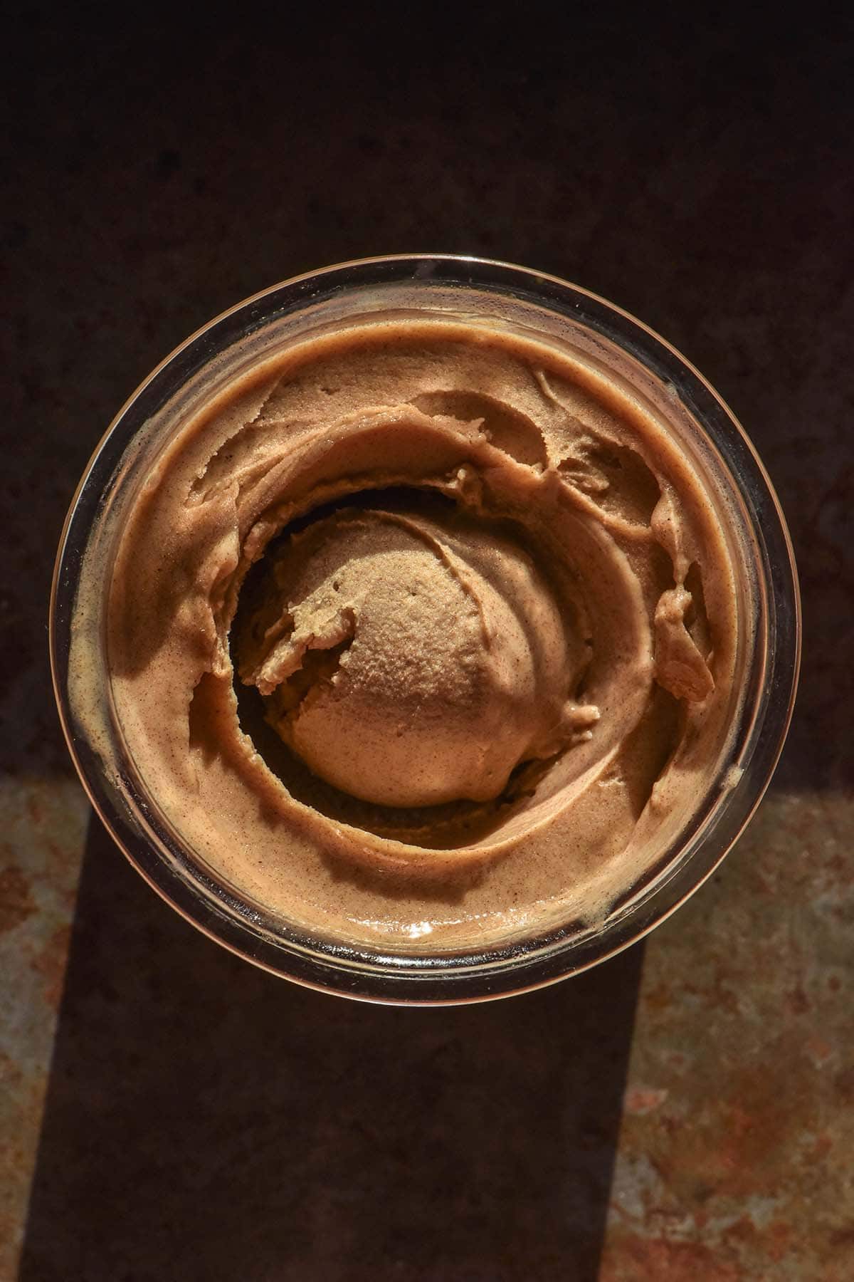 A dark and moody aerial image of a tub of Ninja Creami sticky date pudding atop a dark backdrop